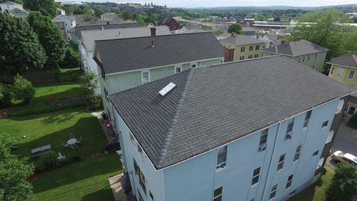 Aerial view of white apartment buildings with gray roofs in a green suburban neighborhood