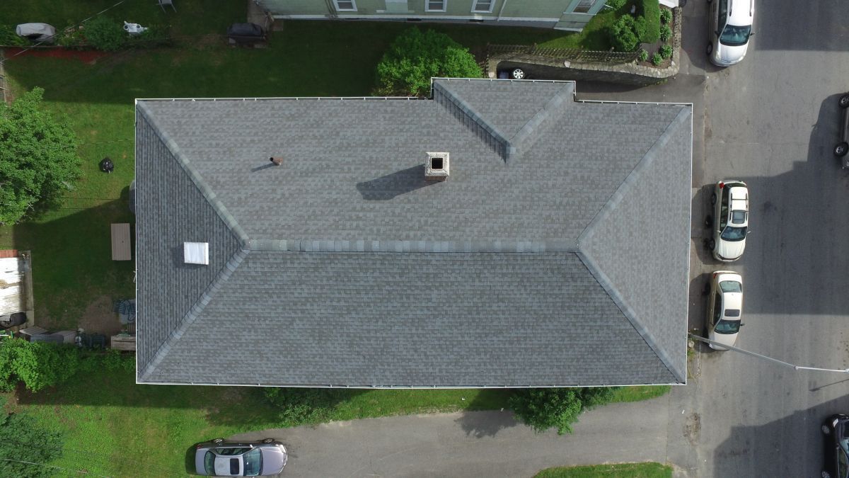 Aerial view of a gray-roofed house with parked cars along a street and driveway.