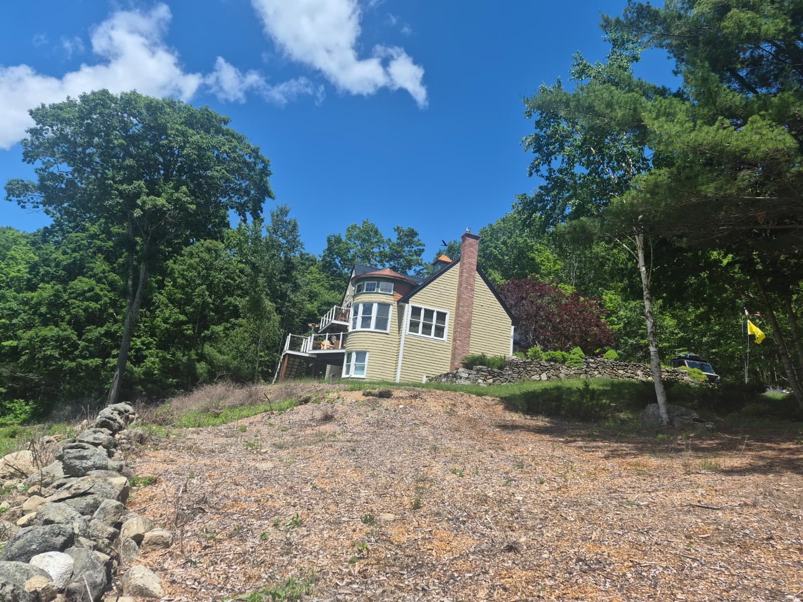 House with stone driveway on a wooded hillside under a bright blue sky