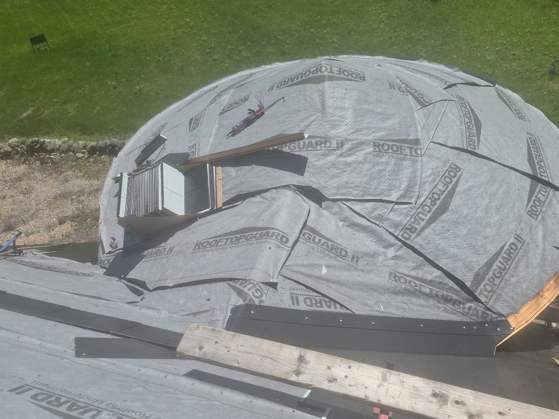 Damaged gray dome tent with broken panels and debris on grass near a road