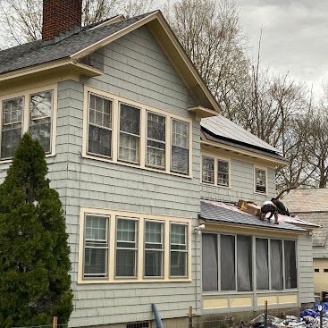 Gray two-story house with workers repairing the lower roof near the side windows