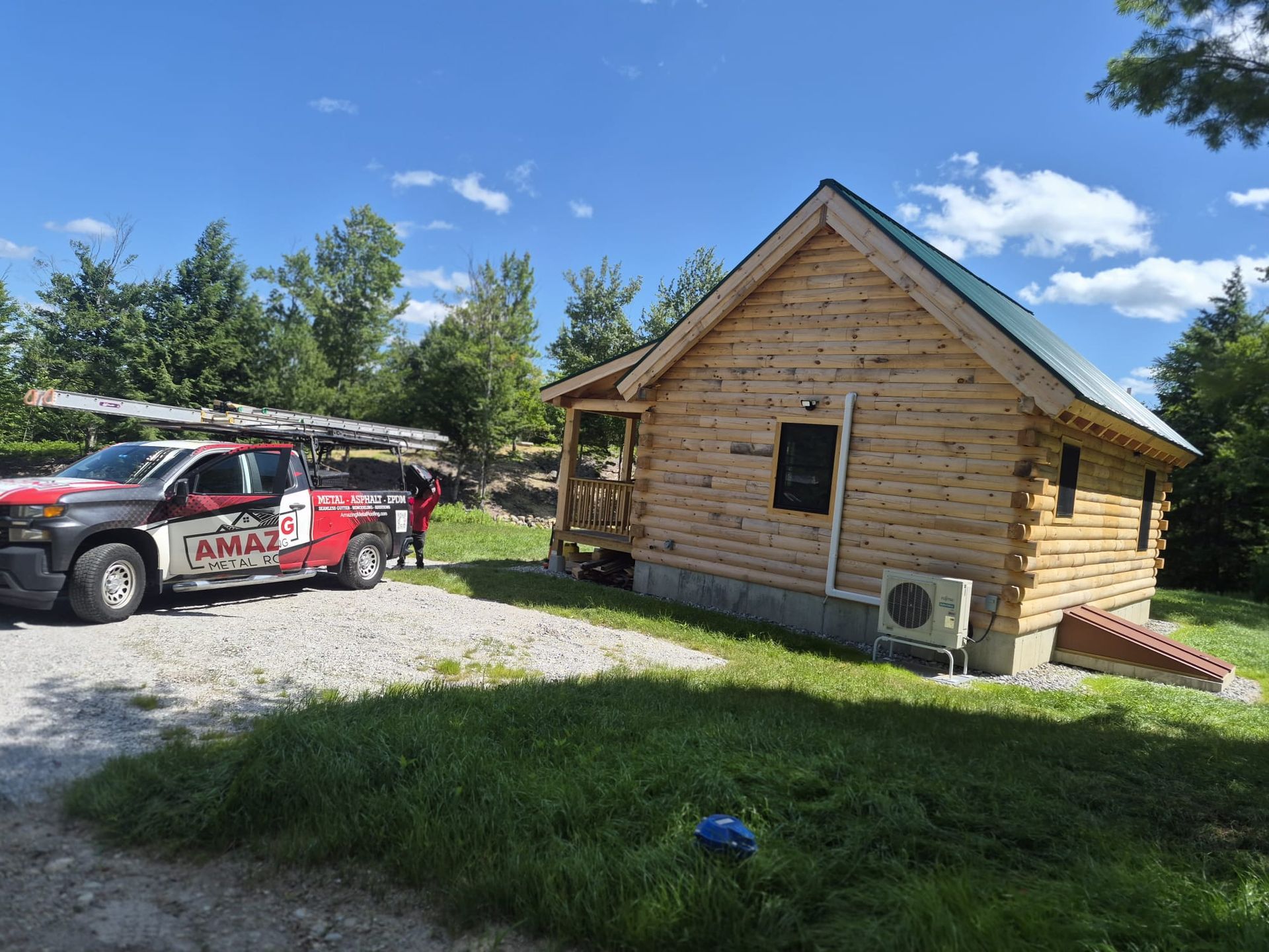 Red SUV parked beside a small wooden cabin under a blue sky with clouds