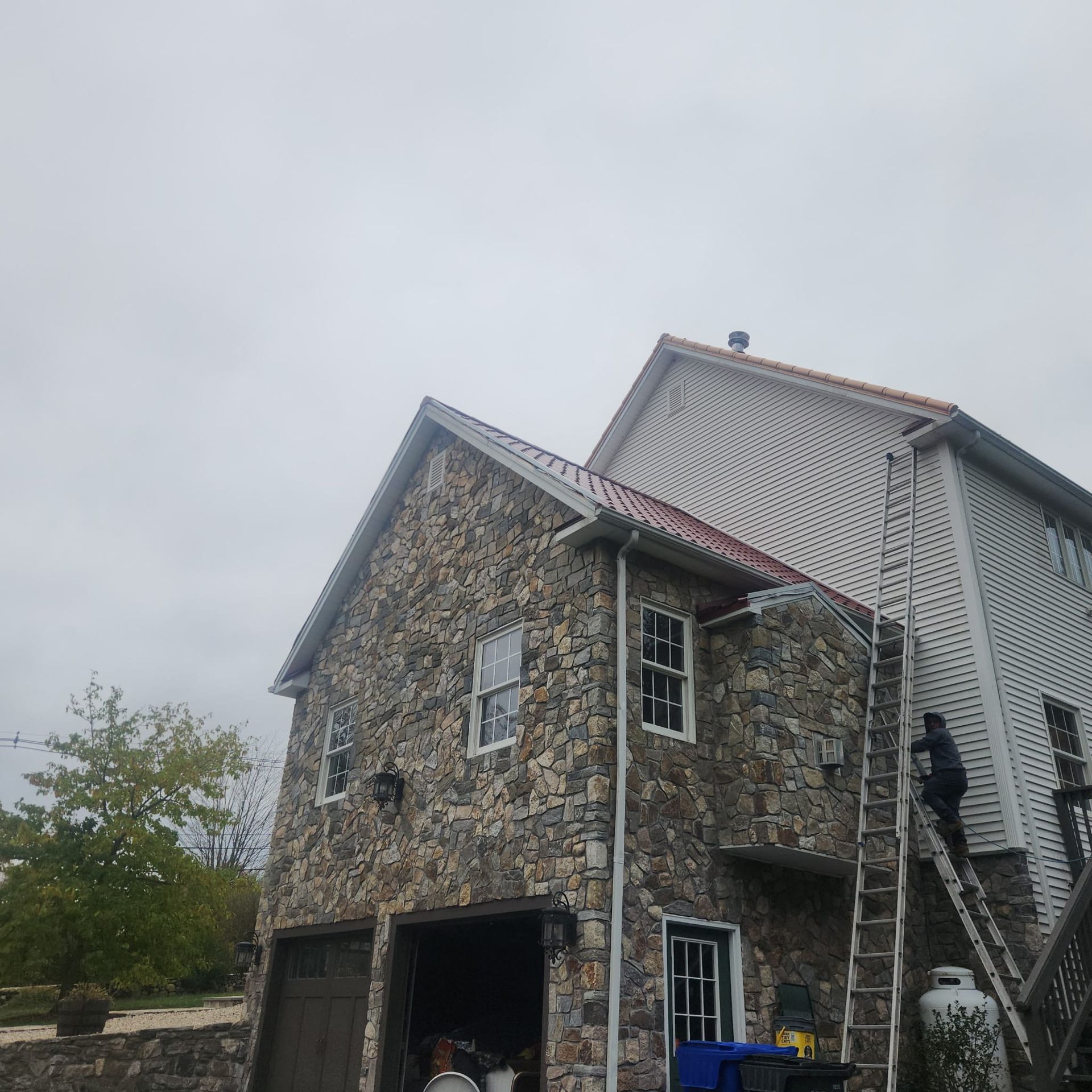Stone garage attached to a gray house, with an exterior staircase and cloudy sky.