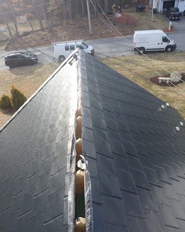 Damaged dark roof ridge with a long gap, viewed from above near parked vehicles and yard below