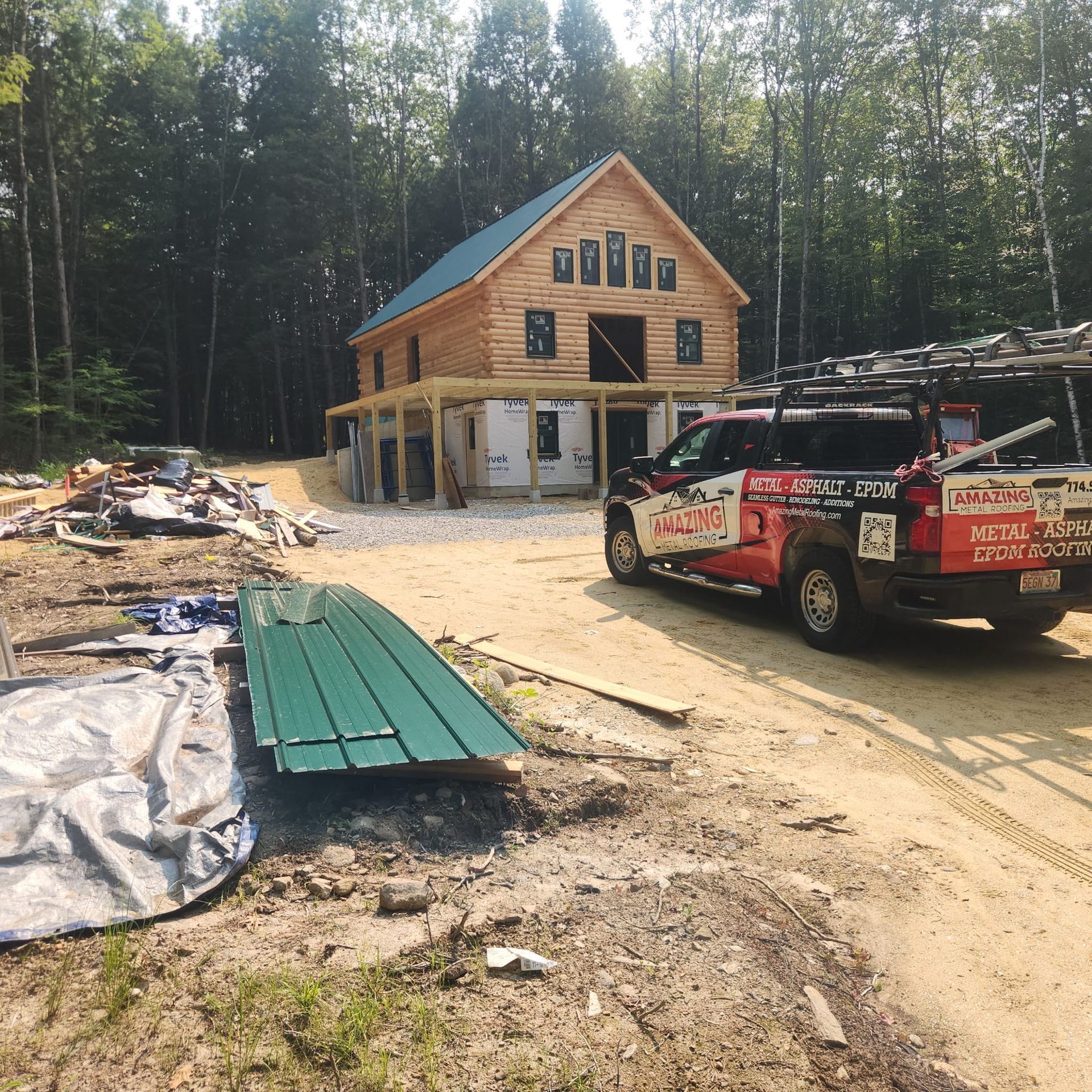 Wooden house under construction with a work truck on a dirt driveway in a wooded area