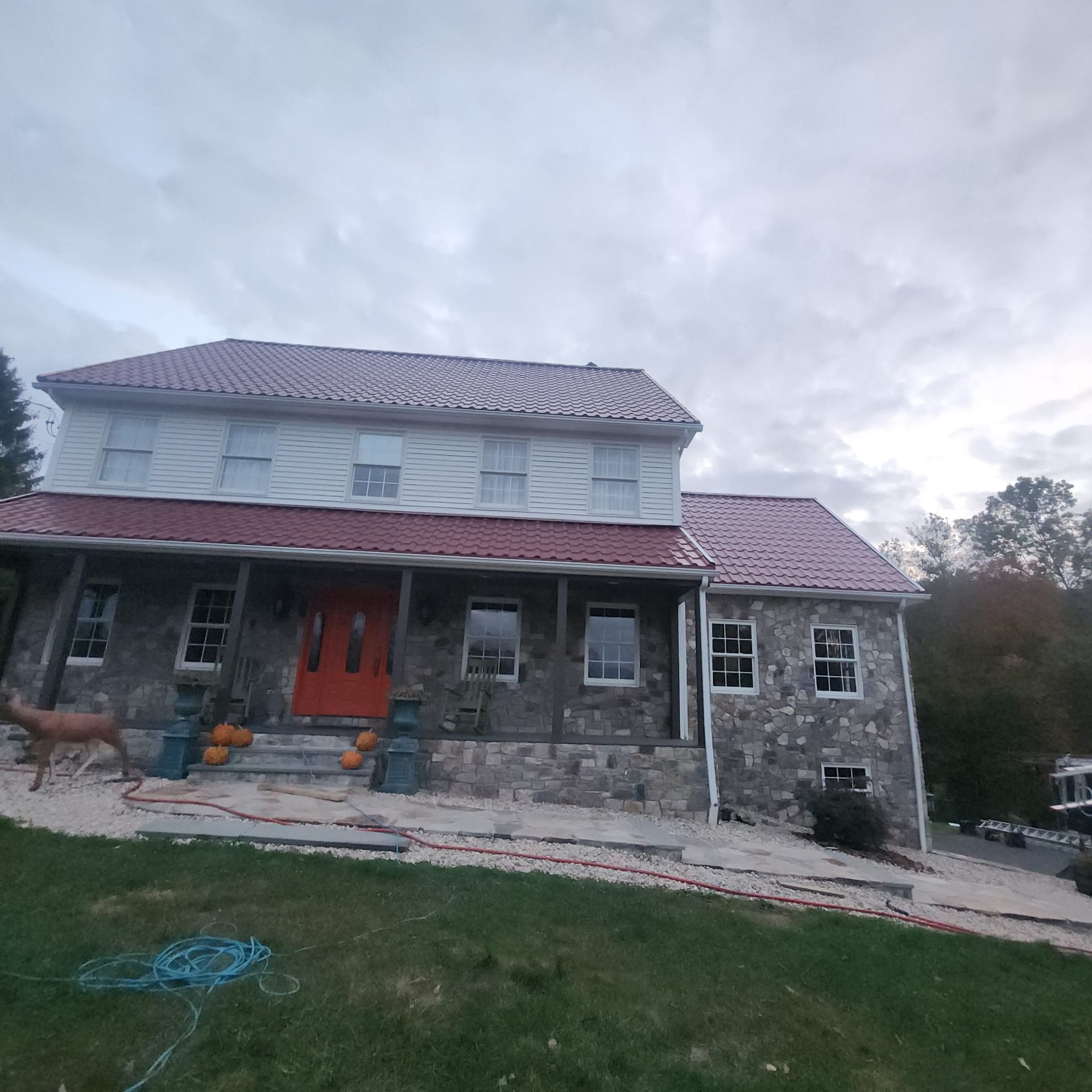 Stone house with red roof, orange front doors, and a dog standing on the front lawn under a cloudy sky