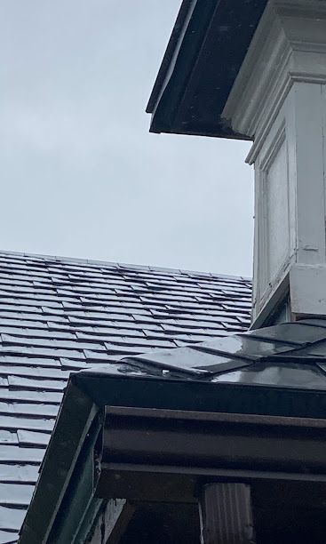 Snow-dusted roof shingles and a house eave against a gray sky
