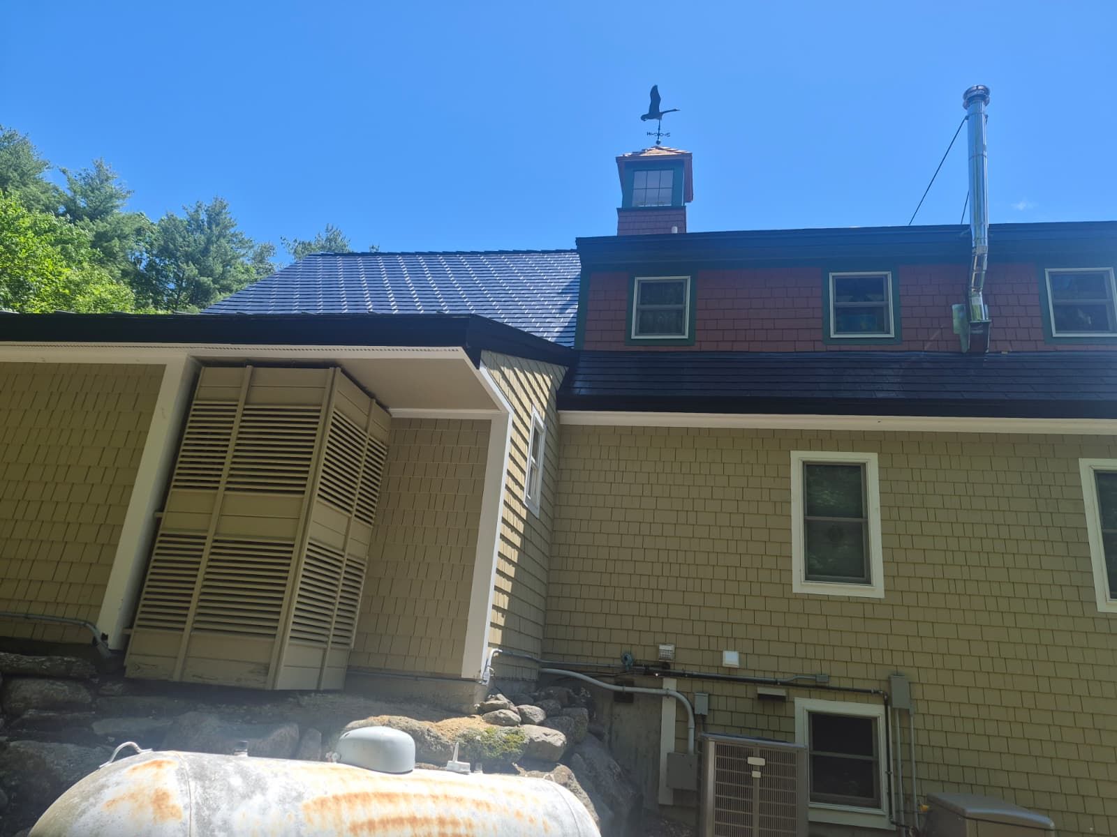 Brick house with slanted solar panels, tan siding, and blue sky above a rooftop vent.