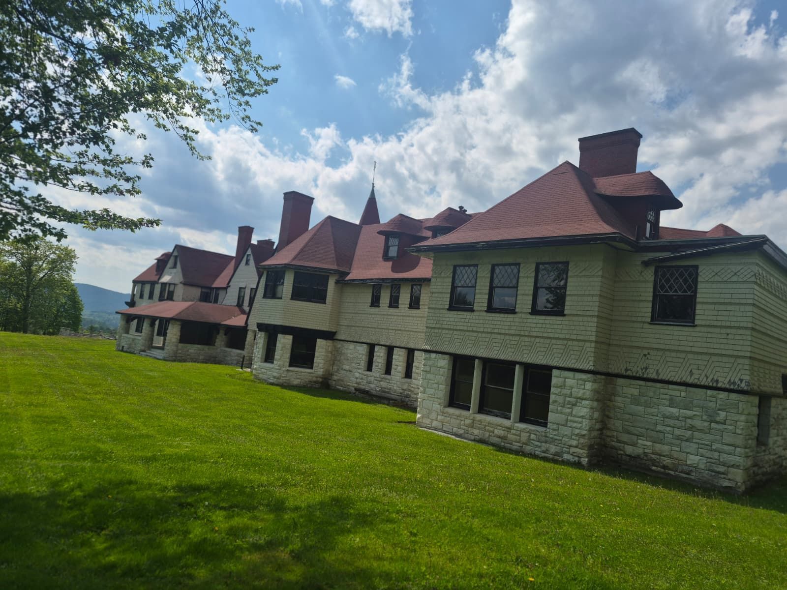 Stone lodge building with red roofs on a green lawn under a partly cloudy sky