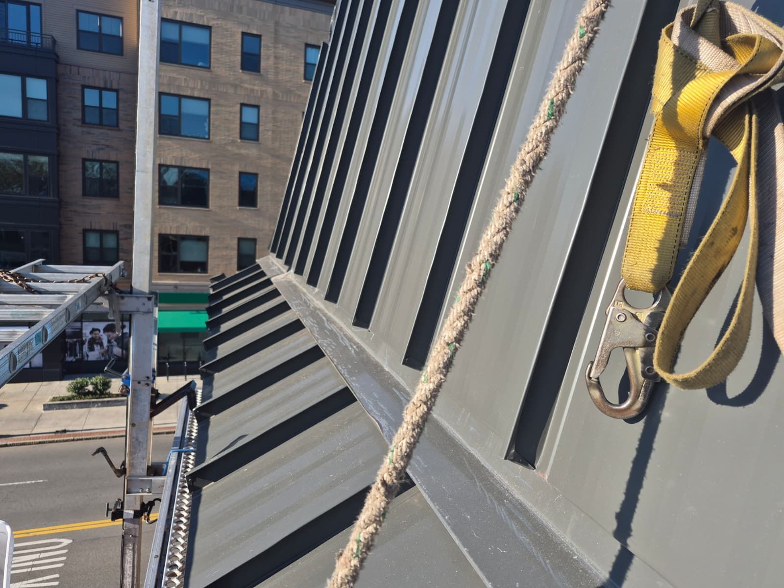 Rooftop view of slanted metal panels and hanging ropes beside a city building.