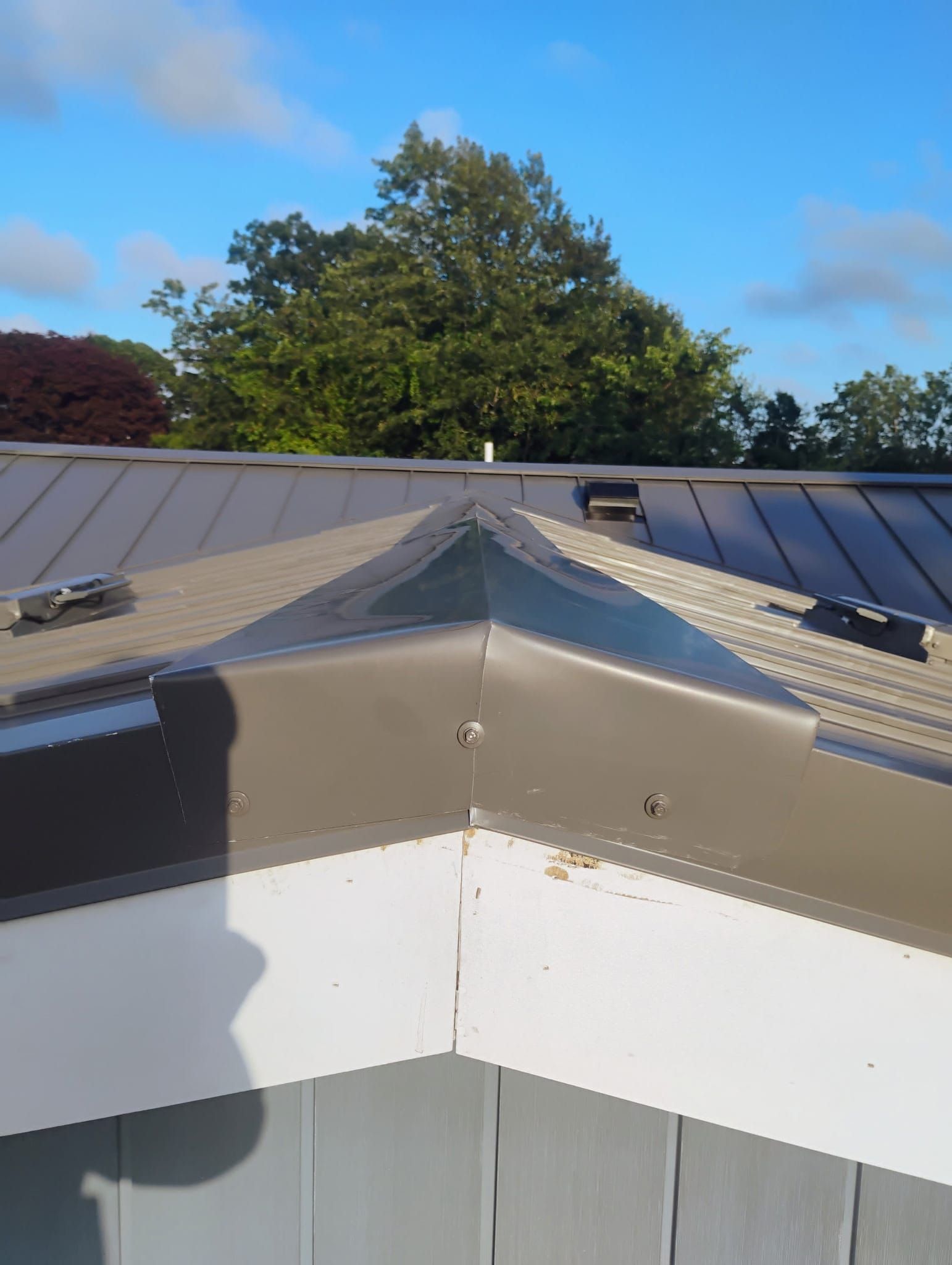 Rooftop corner with gray metal panels and white trim beneath a clear blue sky