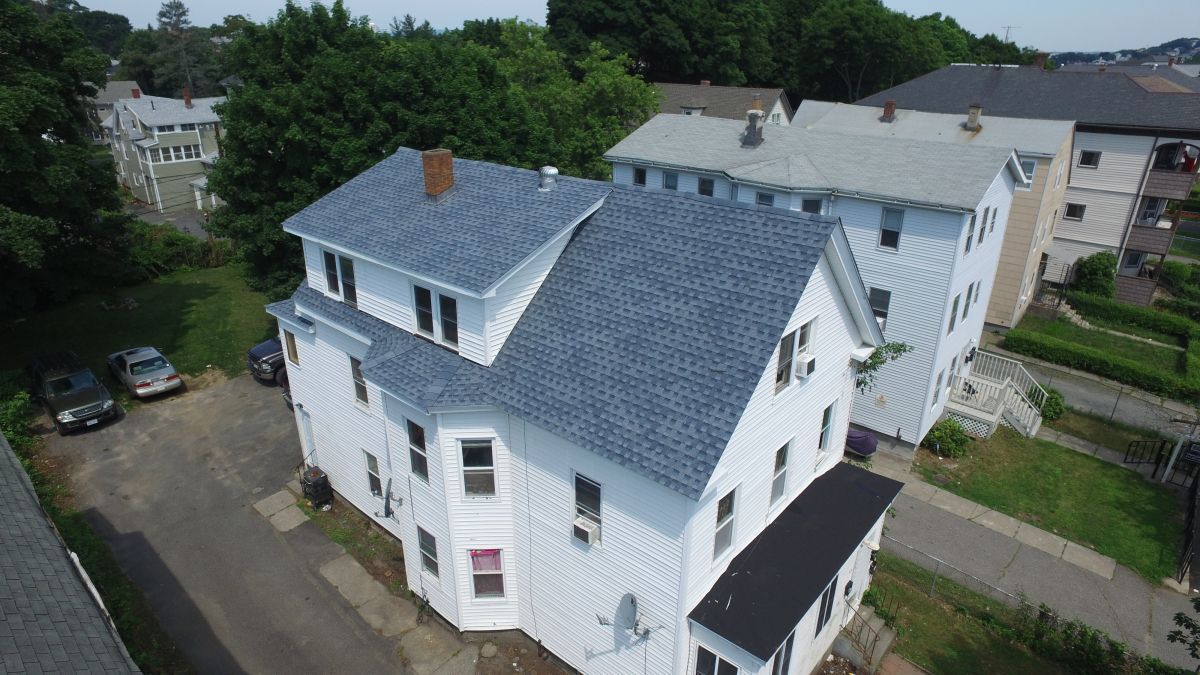 Aerial view of a white apartment building with a blue roof beside a road and trees