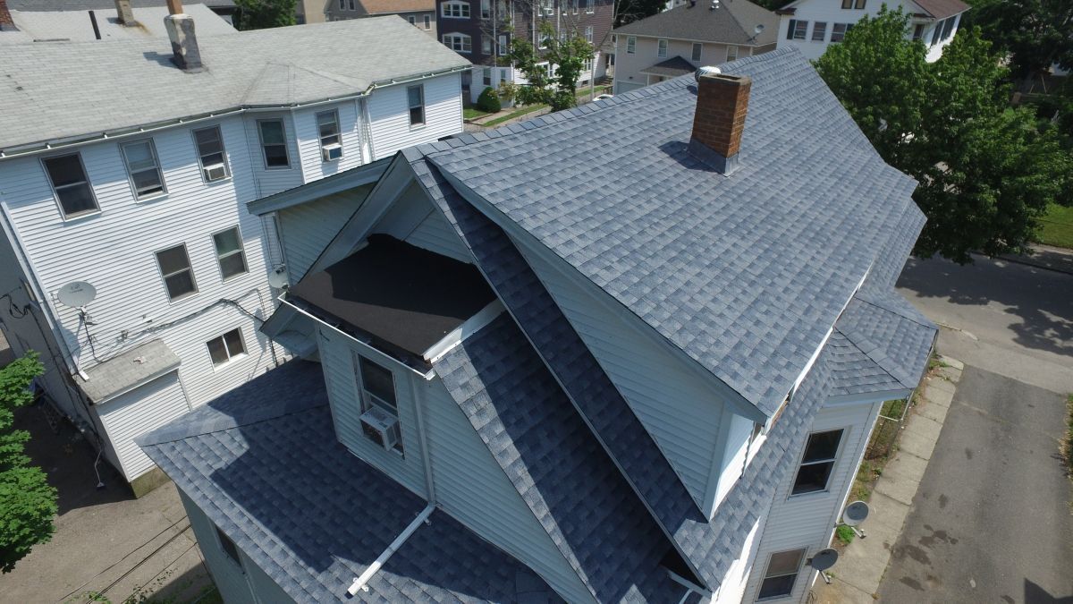 Aerial view of a gray house with a steep roof and neighboring buildings on a residential street