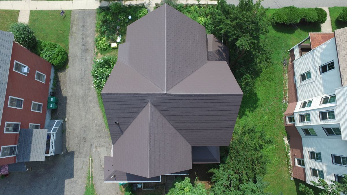 Aerial view of a house with a gray roof surrounded by trees and neighboring buildings