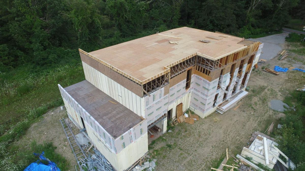 Partially built two-story house with a damaged roof in a wooded rural area