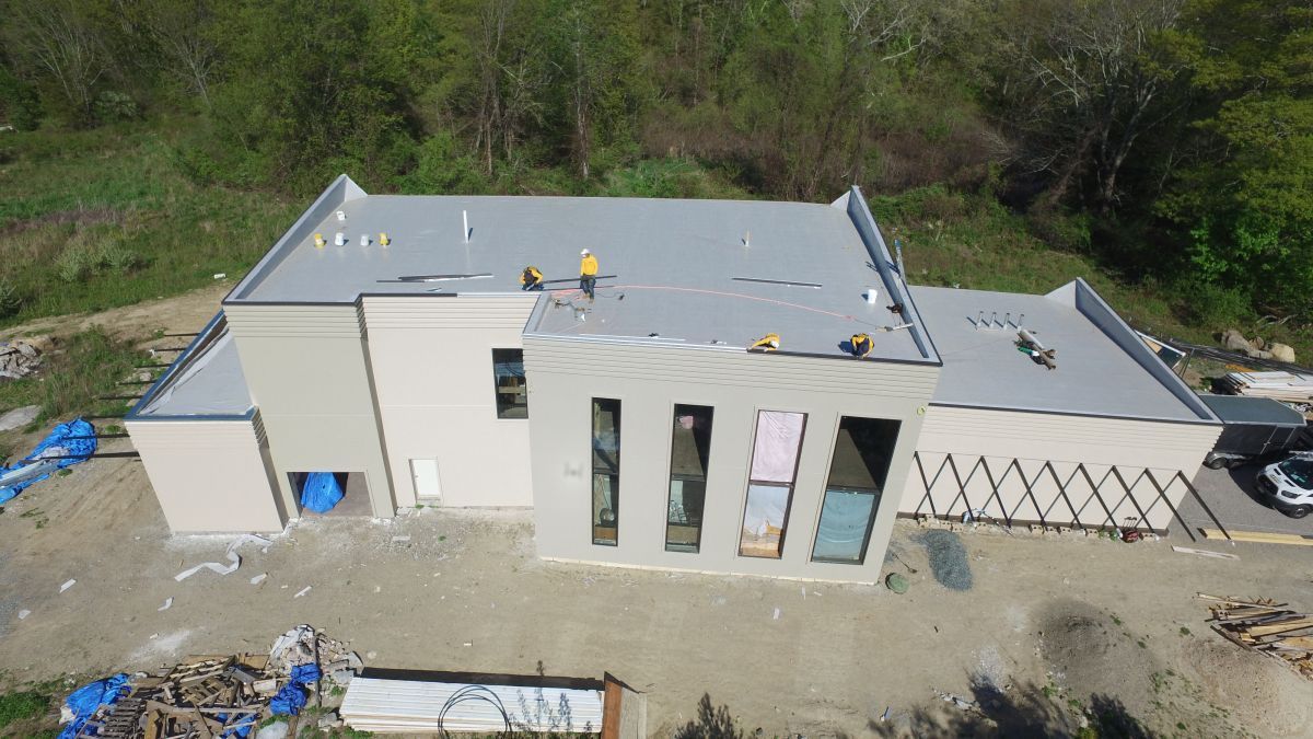 Aerial view of a modern house under construction with a gray roof and unfinished exterior walls.