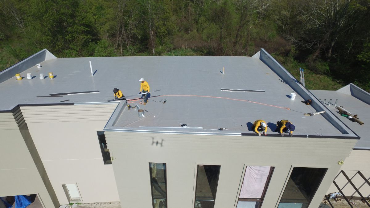 Workers on a flat rooftop installing a gray roof membrane on a building.