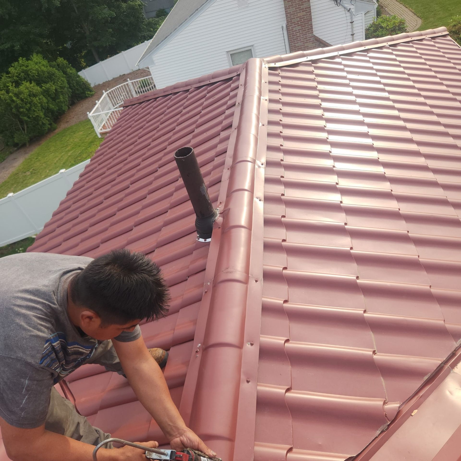 Worker repairing a red metal roof beside a black vent pipe