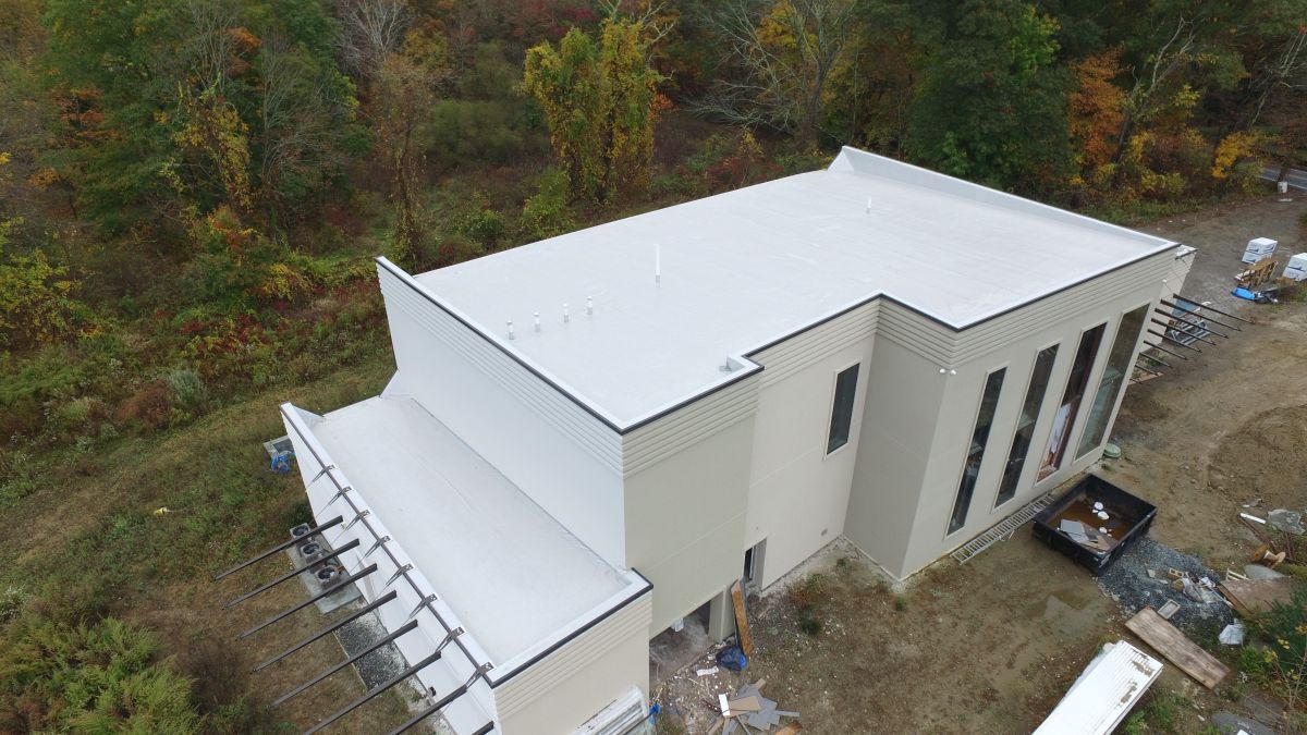Aerial view of a white modern building with a flat roof in a wooded area.