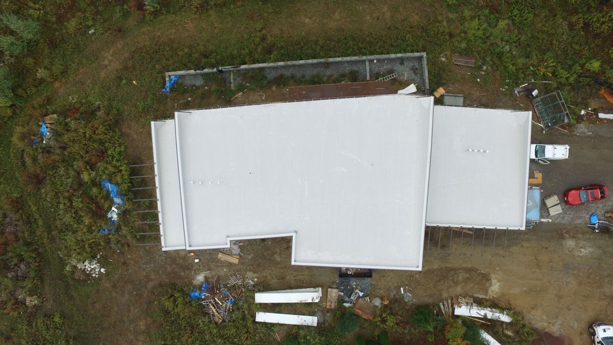 Aerial view of a white-roofed building with a small side structure and dirt surrounding it.