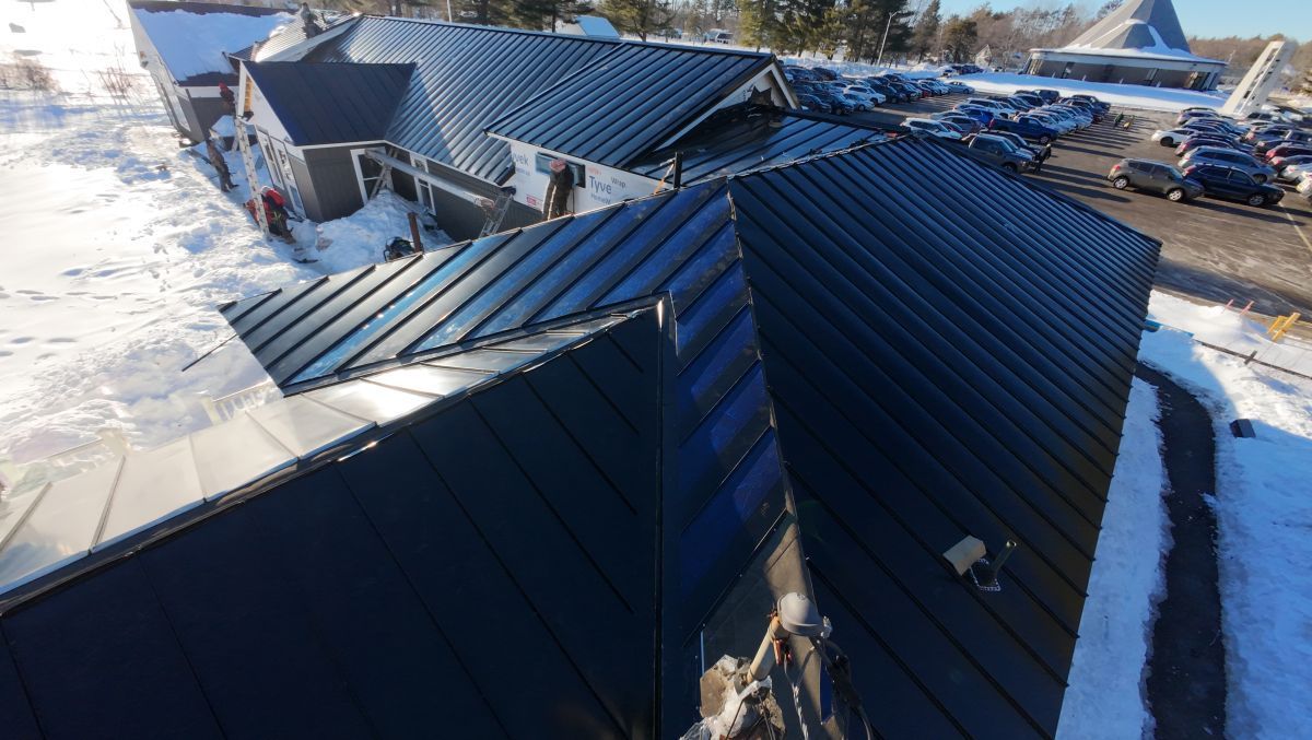 Snow-covered blue metal roofs with visible damage and debris in a winter scene