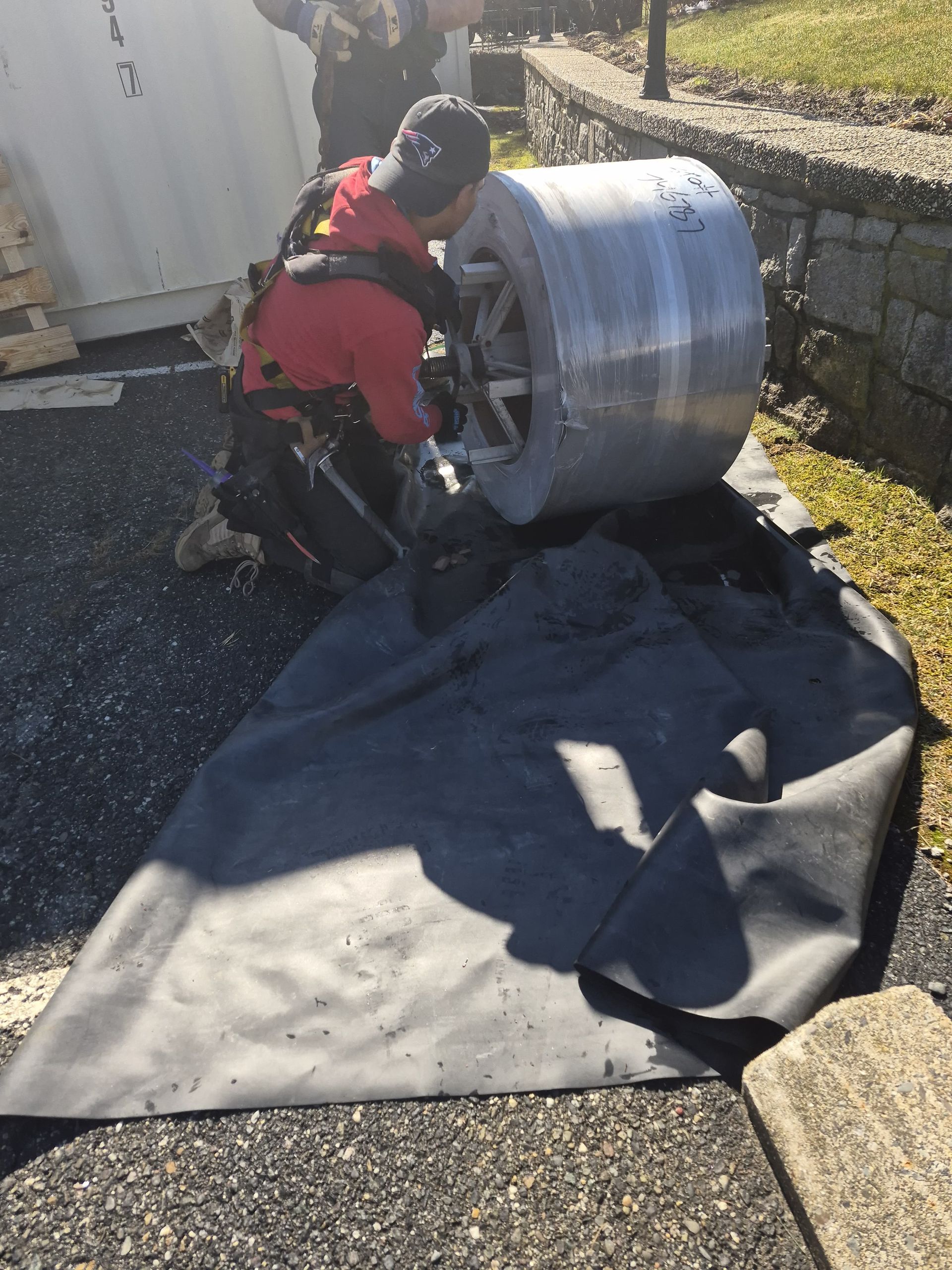 Worker in red jacket kneeling beside a large metal duct on a rooftop