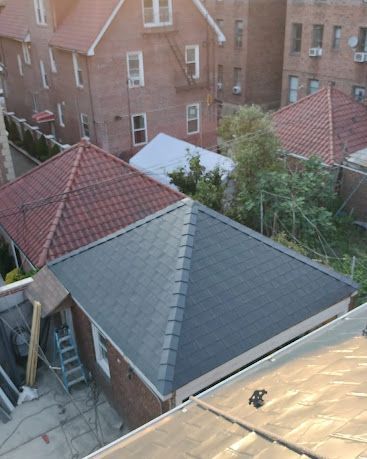 Rooftops and brick apartment buildings viewed from above, with a dark gray roof in the foreground.