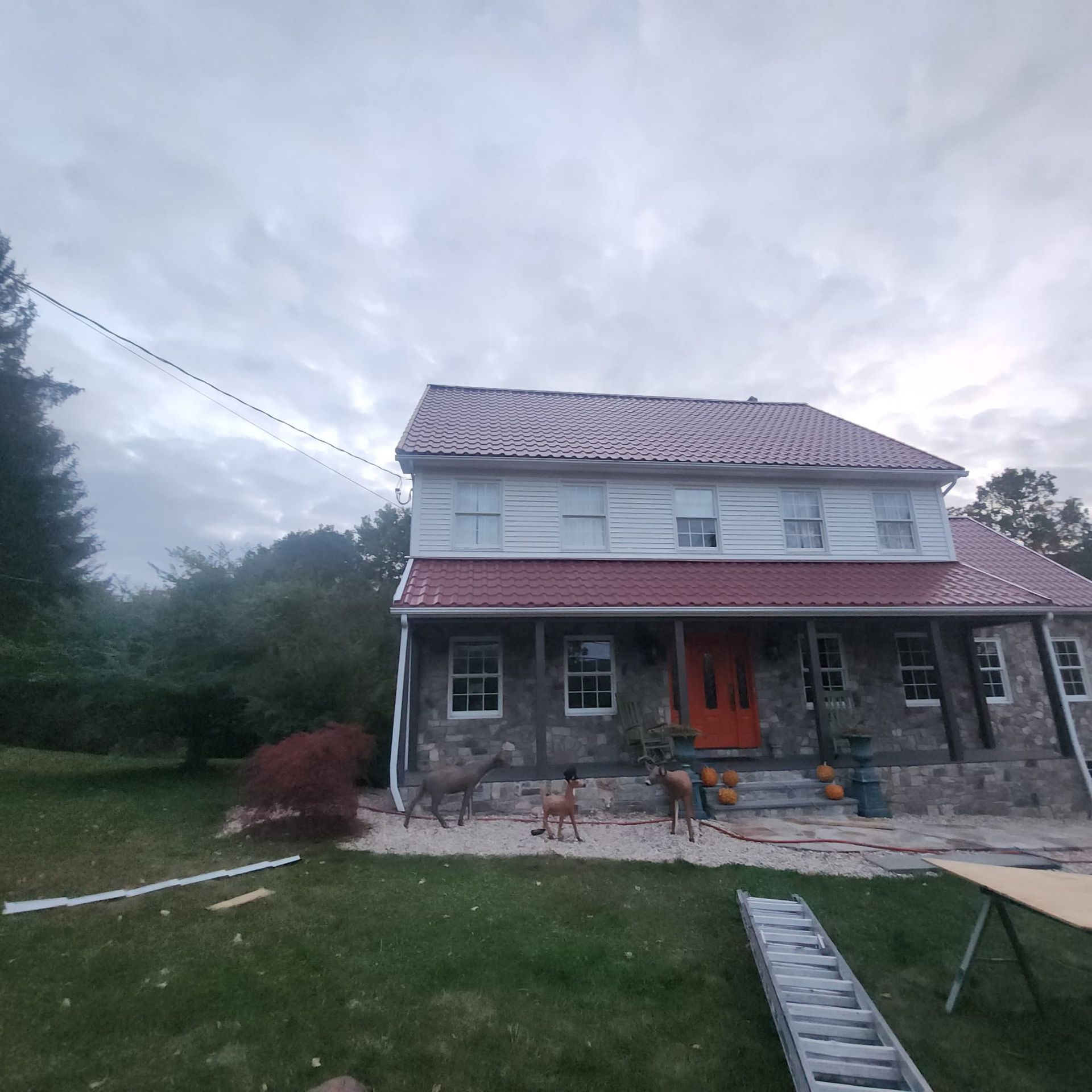 Two-story stone house with red roof and orange door, seen from a grassy yard at dusk
