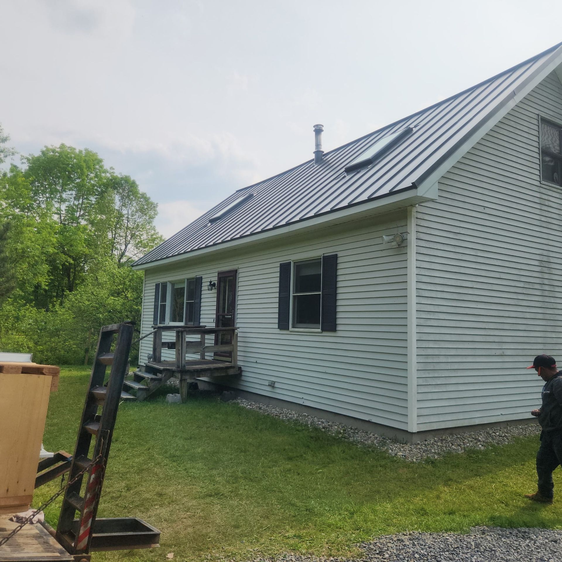 White house with gray metal roof and porch in a grassy yard, with a person standing at right