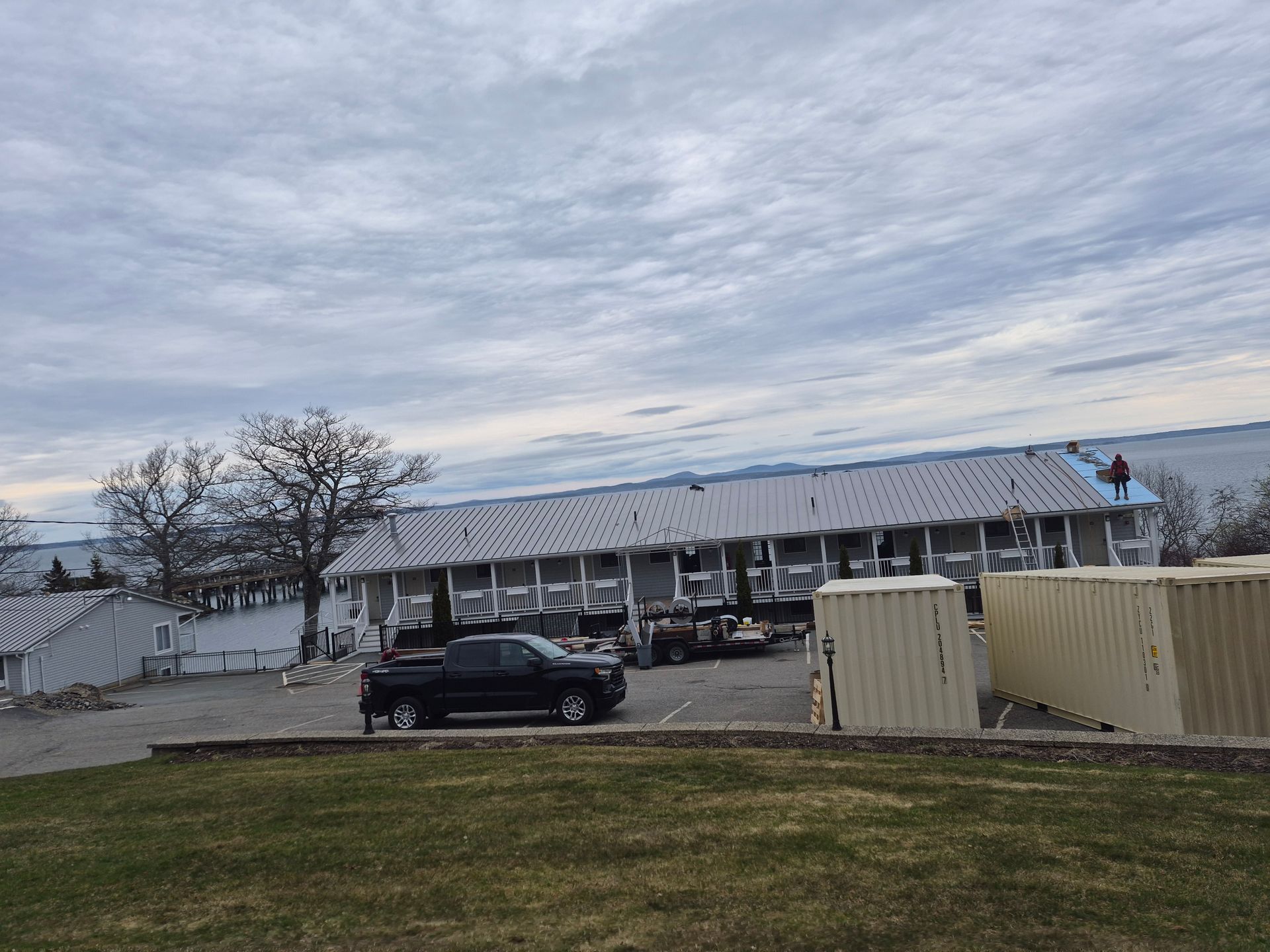 Snowy parking lot with a long white building, parked black car, and cloudy winter sky