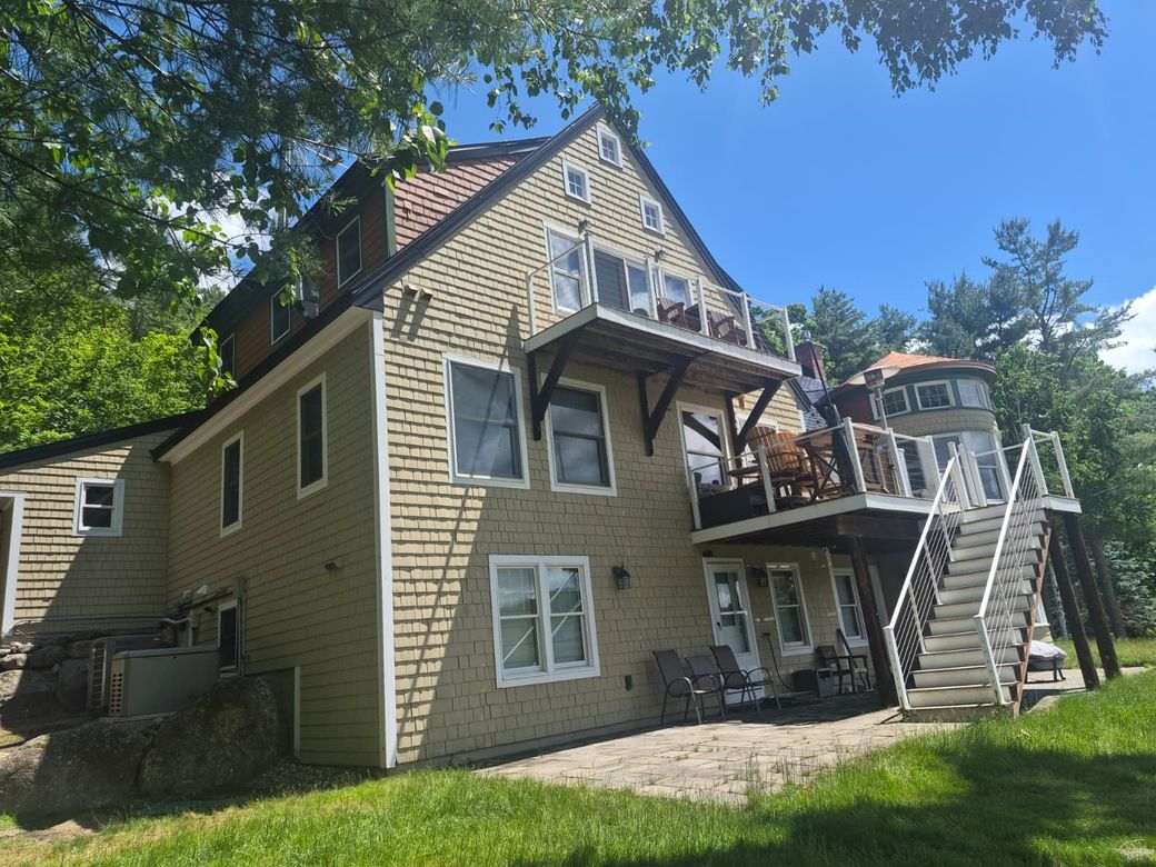 Beige two-story house with balconies and exterior stairs, seen from the yard under a blue sky.