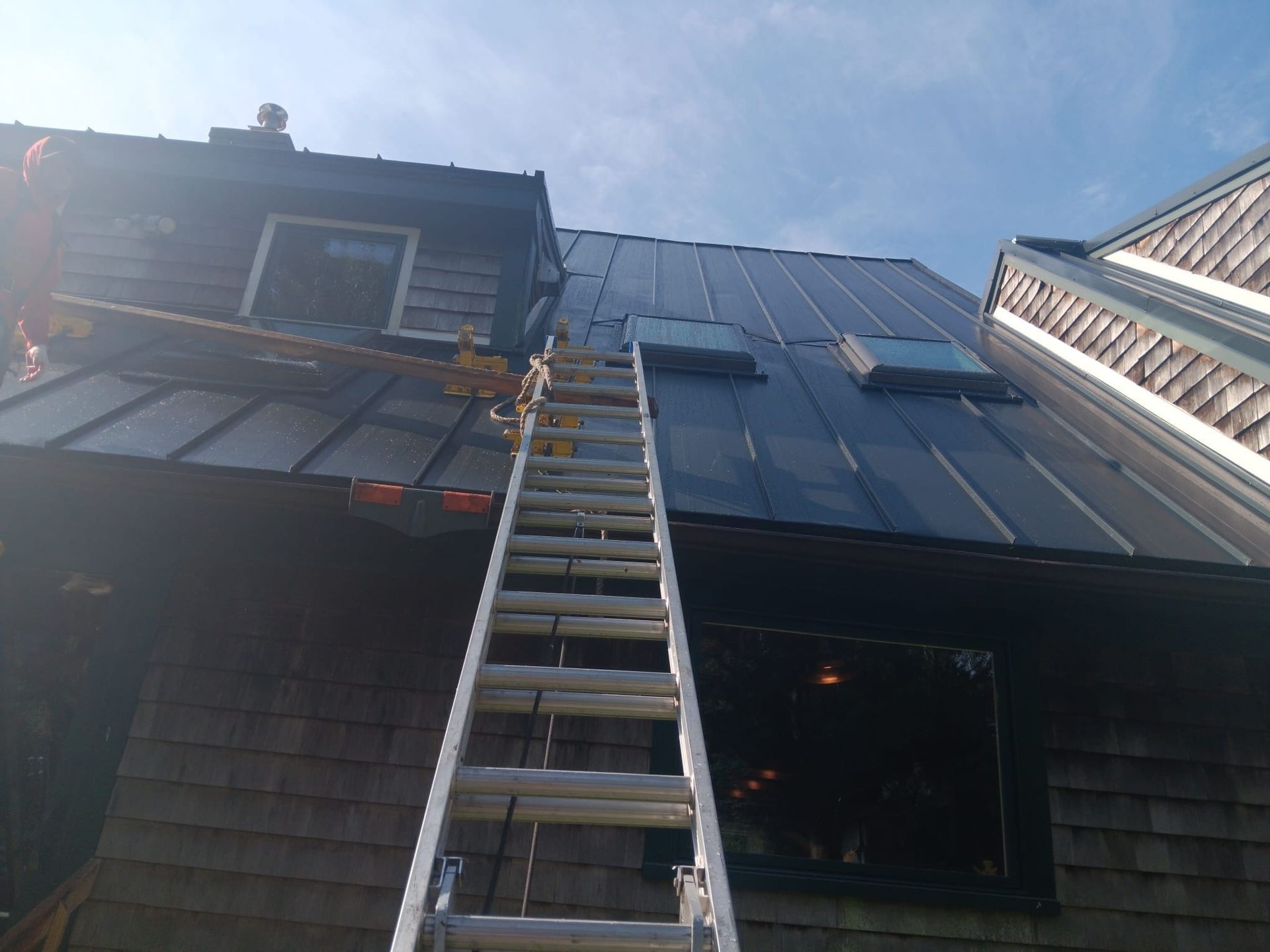Ladder leaning against a house roof with solar panels, viewed from below.