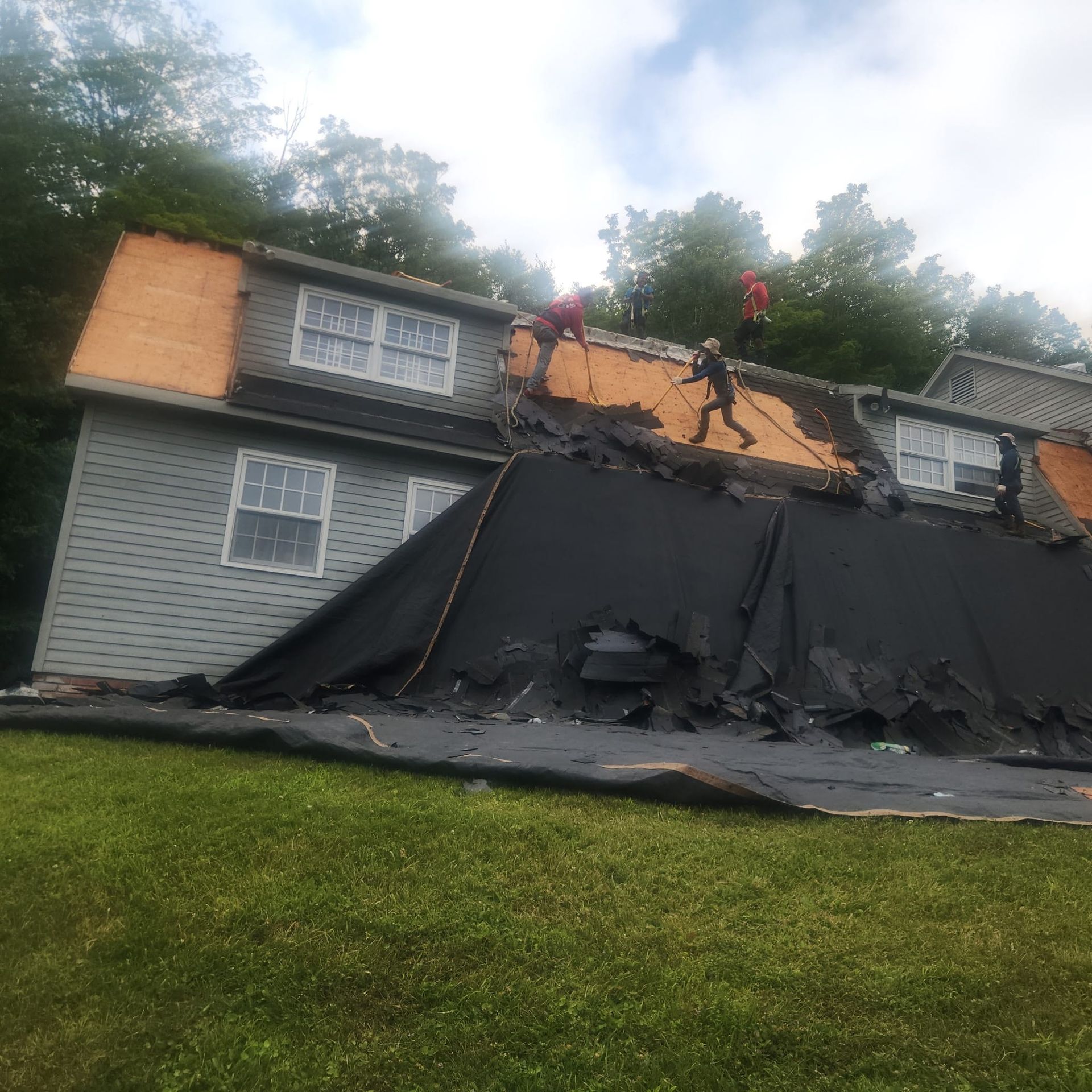 Damaged house roof with black tarp and workers boarding it after storm damage