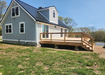 Gray house with a small wooden deck and stairs, viewed from the yard on a sunny day
