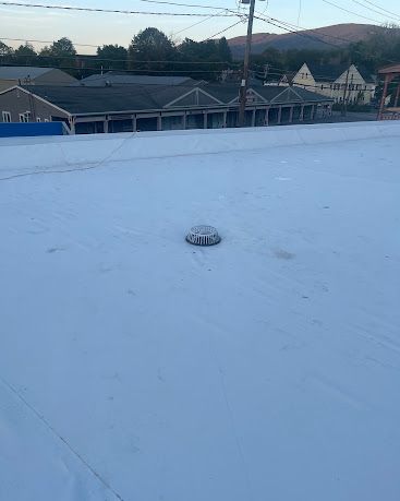 Snow-covered rooftop with a small vent, overlooking houses and hills at dusk