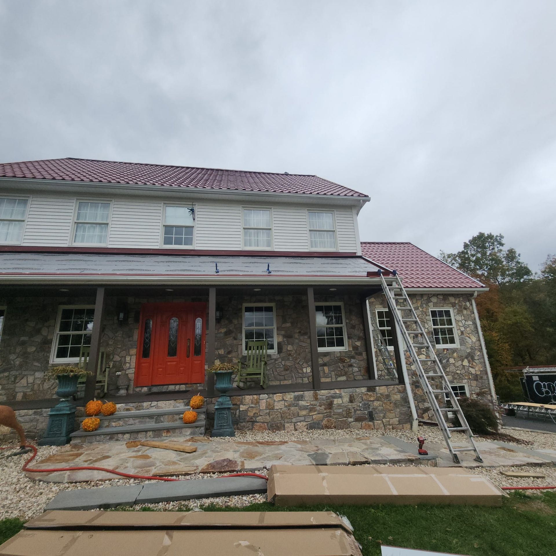 Stone house with red roof and porch, front door, and two ladders leaning against the front and side.