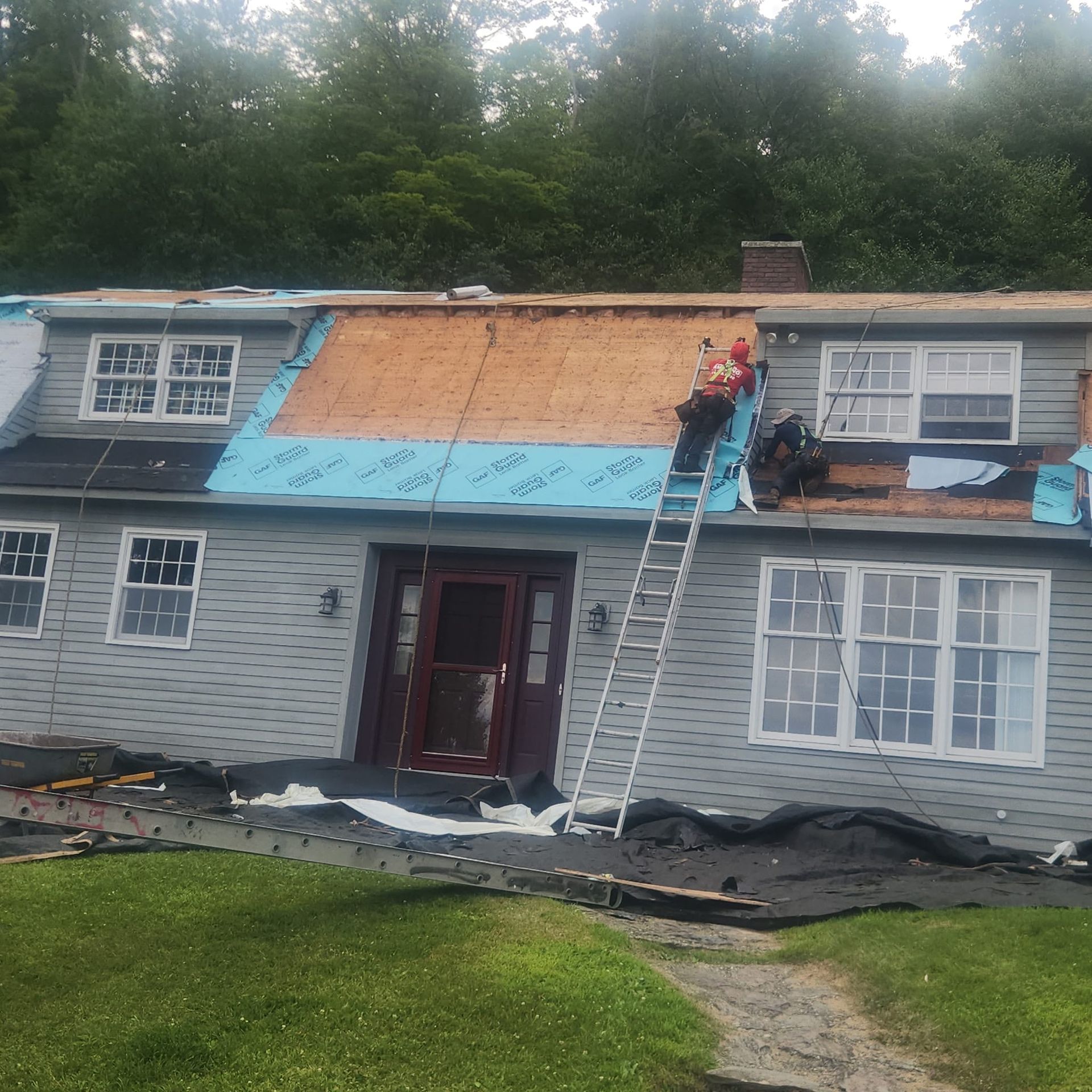House roof under repair with worker on ladder, blue tarp, and exposed plywood