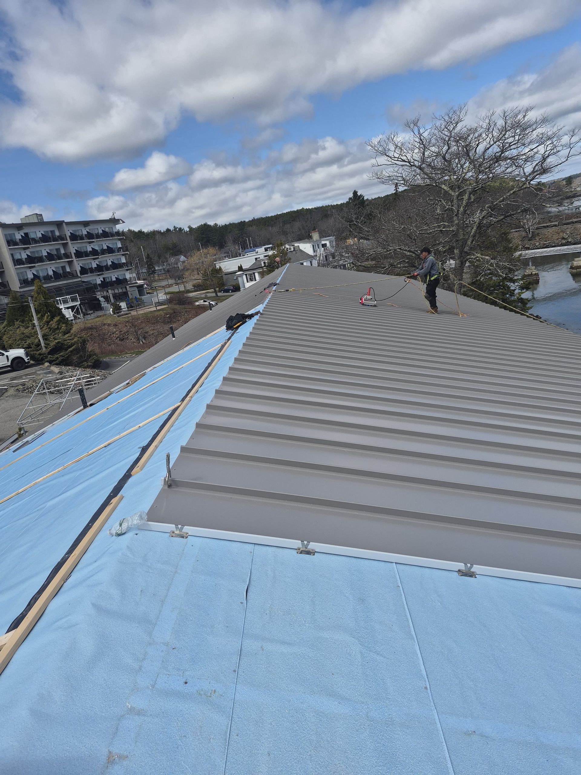 Roofing work on a corrugated roof, with blue underlayment and a cloudy sky in the background