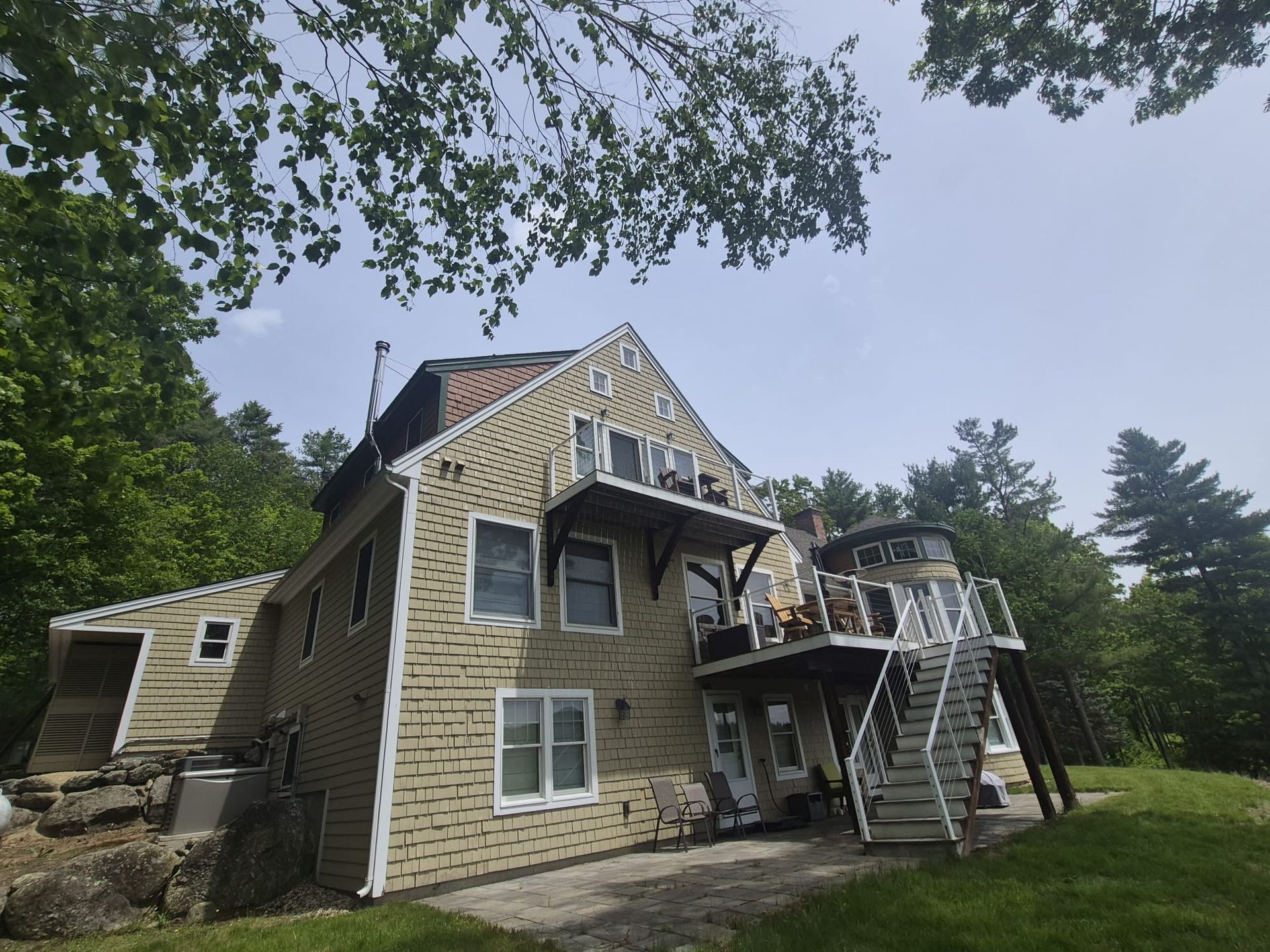 Stone house with gabled roof and exterior stairs, surrounded by trees under a cloudy sky
