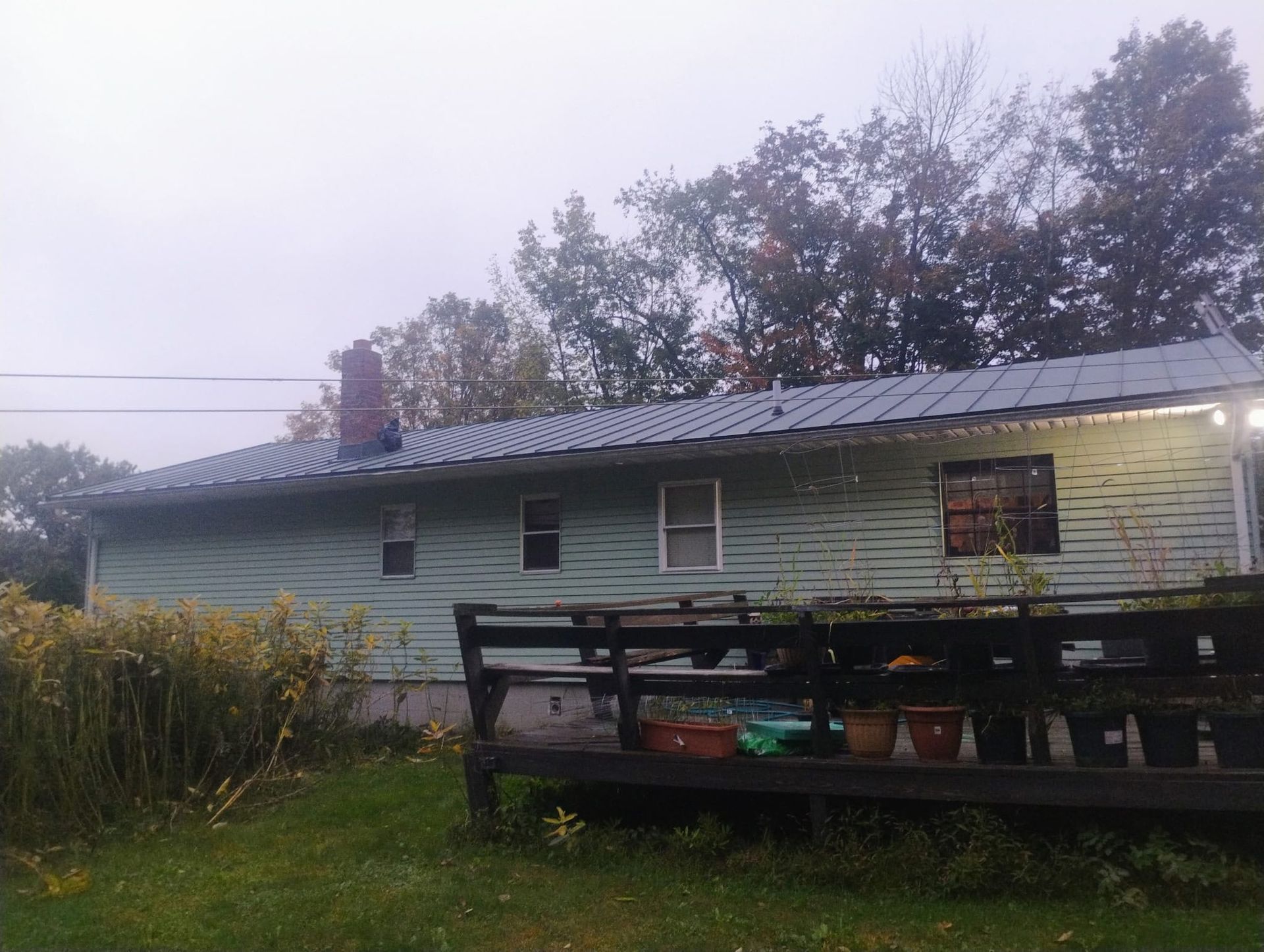 Long white mobile home with a dark roof and porch in a grassy yard at dusk