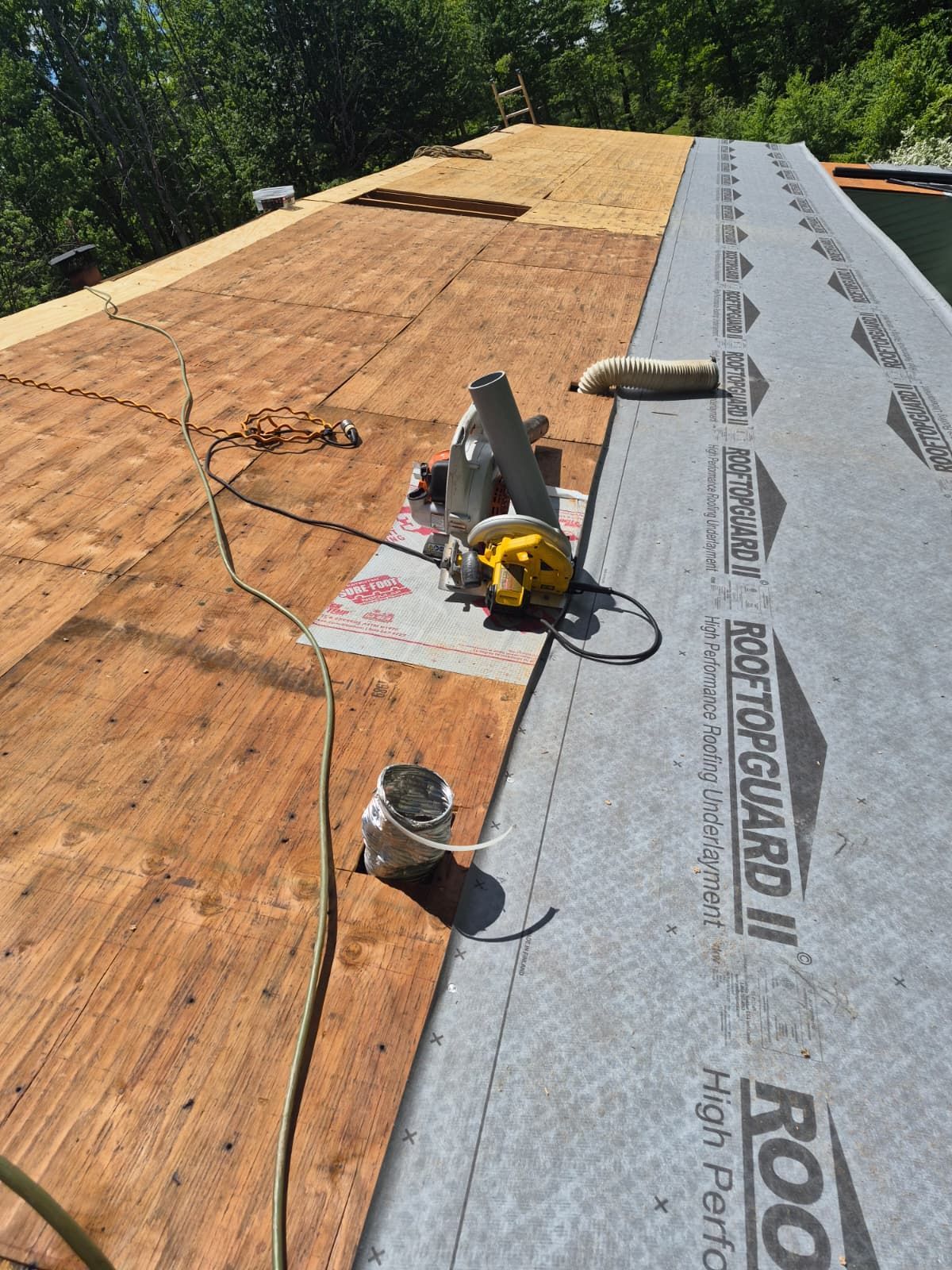 Roof under construction with gray underlayment, exposed plywood, and a circular saw near the ridge
