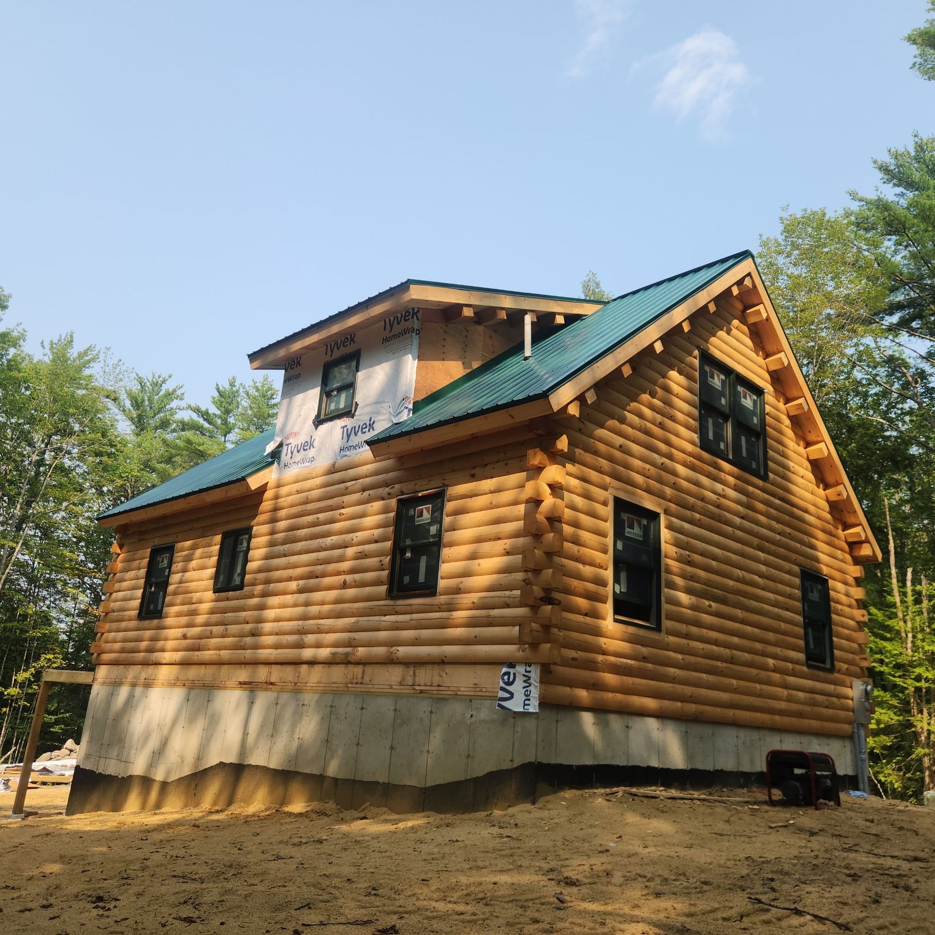 New log-style house with green roof and concrete foundation in a wooded clearing