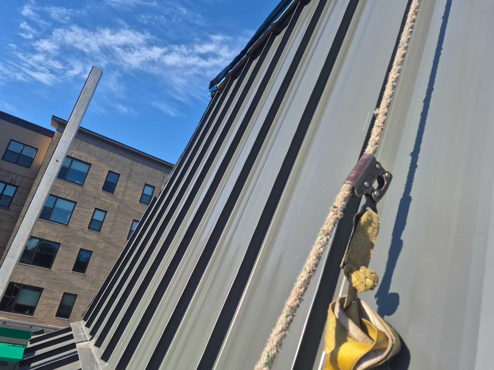 Climbing rope and harness on a tall building facade beside another office building under a blue sky