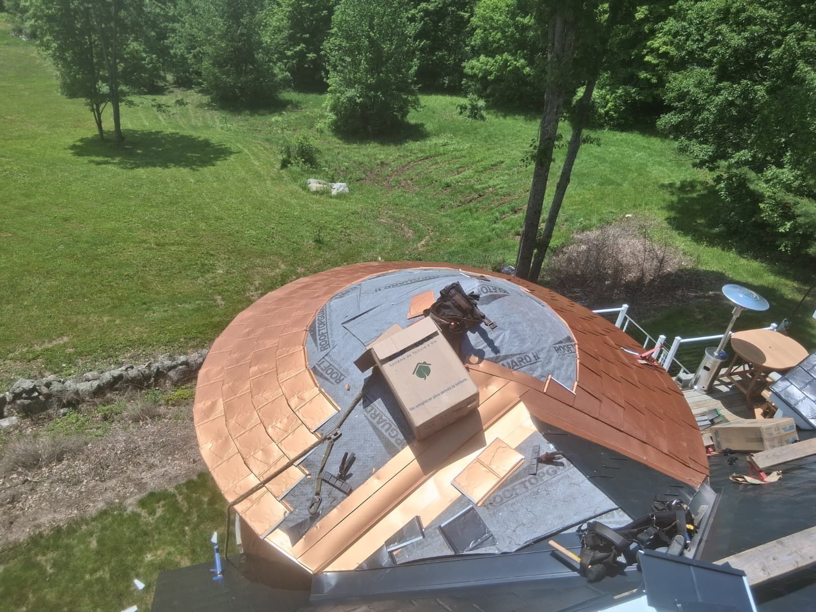 Copper roof under construction with gray underlayment, tools, and a grassy yard behind it
