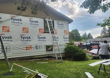 Tyvek-wrapped house under construction with ladders and a worker in the yard