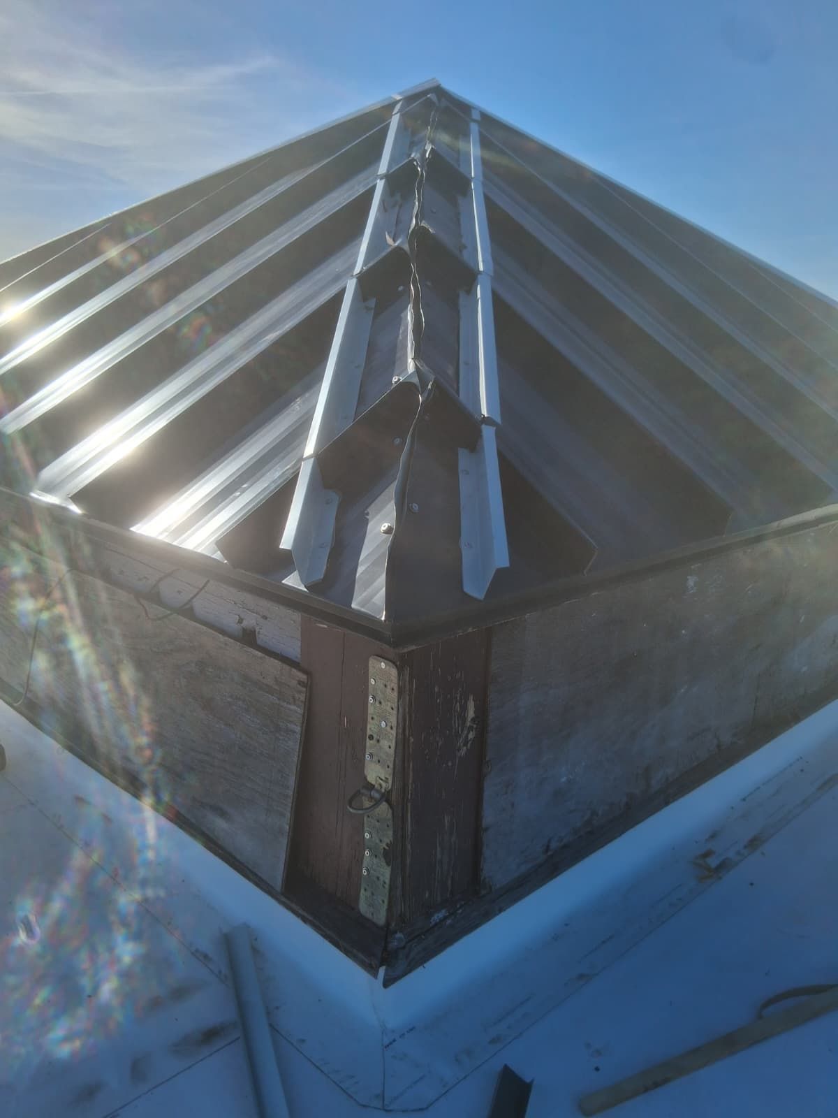 Snow-covered glass roof corner with sunlight reflecting off metal framing