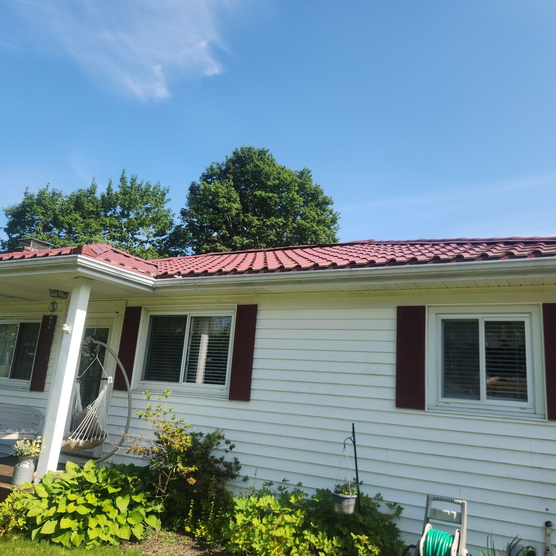 White house exterior with red roof, porch, windows, and green garden under a blue sky