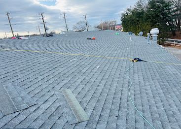 Workers on a sloped roof installing gray shingles with safety ropes visible