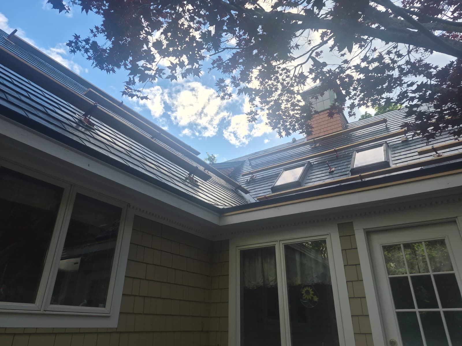 Roofline and chimney framed by trees and blue sky above a house exterior