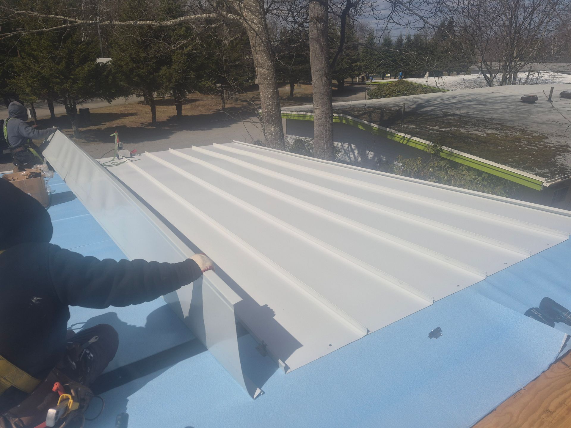 Worker installing white corrugated roof panels on a blue rooftop outdoors